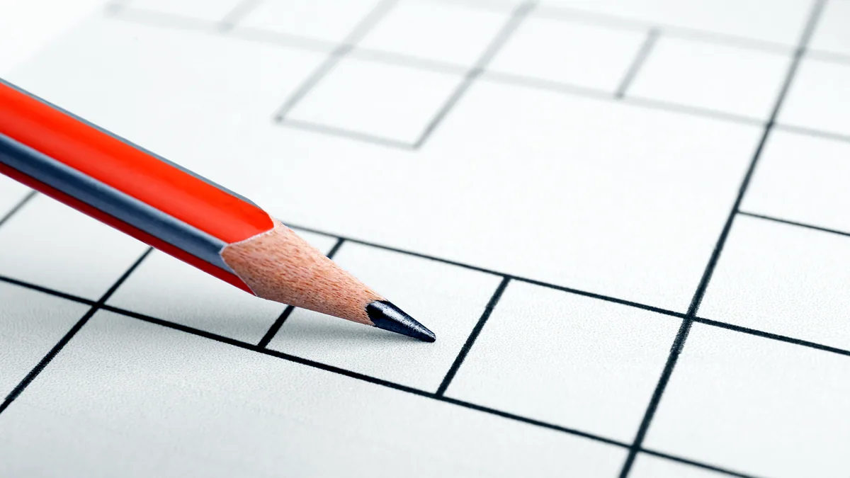A pencil resting on a printed crossword grid, a few squares already filled in.
