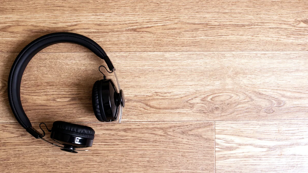 Over-ear headphones resting on a wooden desk beside a notebook and a coffee mug.