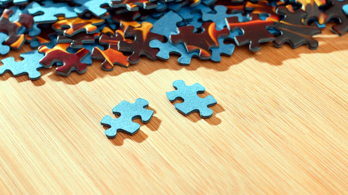 A jigsaw puzzle half assembled on a bright wooden table, pieces scattered around.